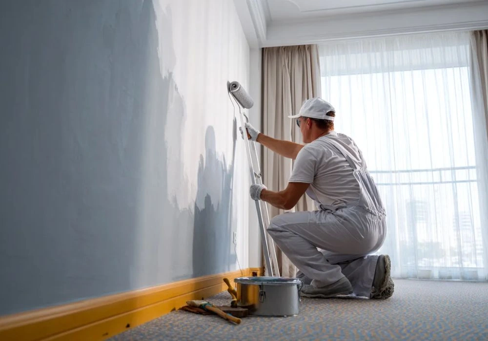 Professional painter applying fresh grey paint to an interior wall.